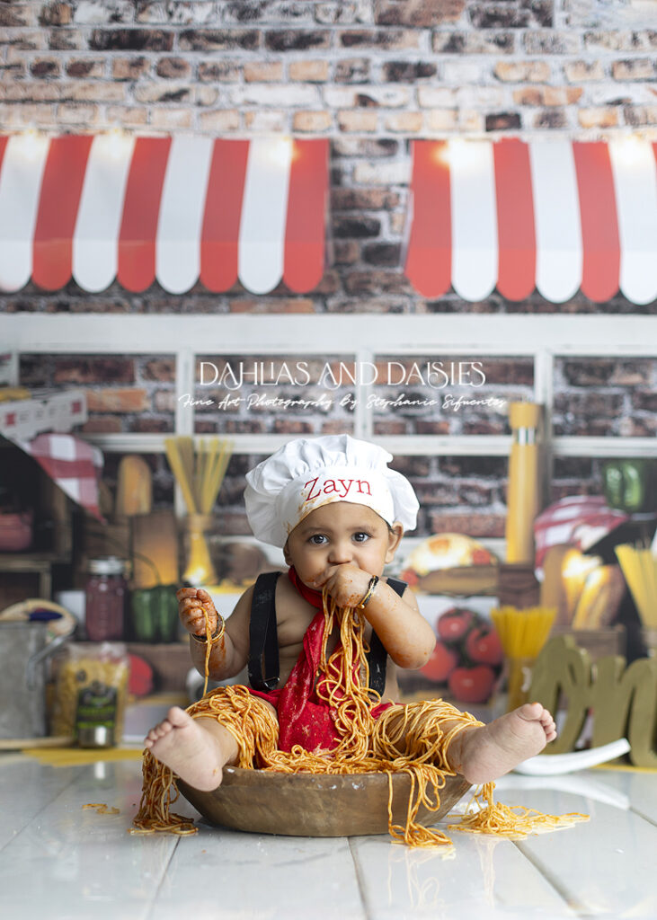 Baby wears chef costume while eating spagetti
