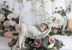 Newborn girl sleeps in circular floral hanging basket