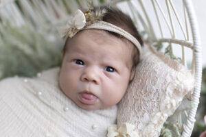 Newborn girl wrapped in beige looks into camera