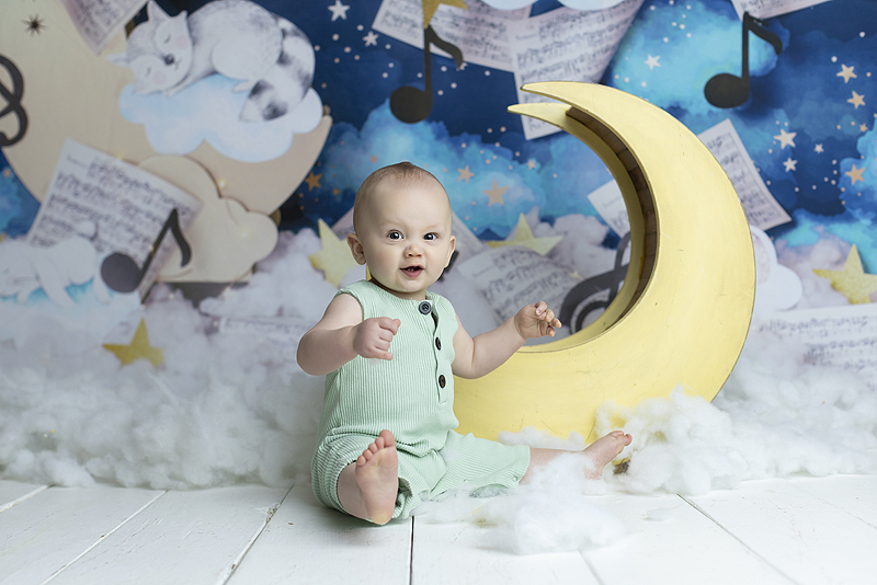 6 month old boy smiles in front of wooden moon prop
