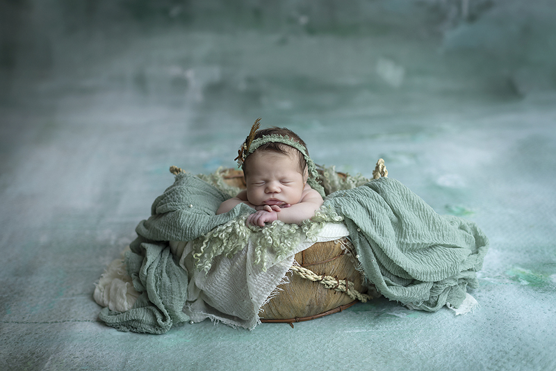 Newborn girl sleeps in basket against mint background