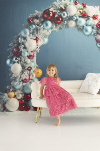 Pretty toddlers sits on white couch in front of colorful ornament arch