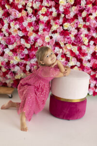 Young girl strikes a post in front of pink lower wall
