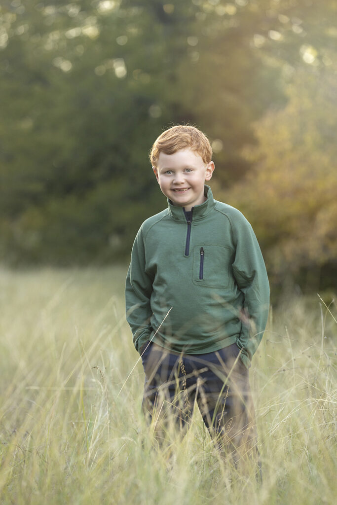 Young boy smiles at camera standing in tall grass