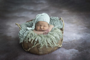 Newborn boy poses in baskets surrounded by mint green fluff