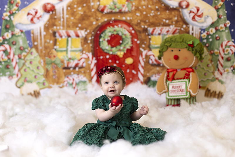 Baby holds ornament in front of gingerbread house