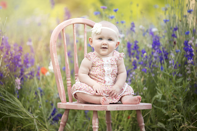 baby girls sits on chair in wildflwoers