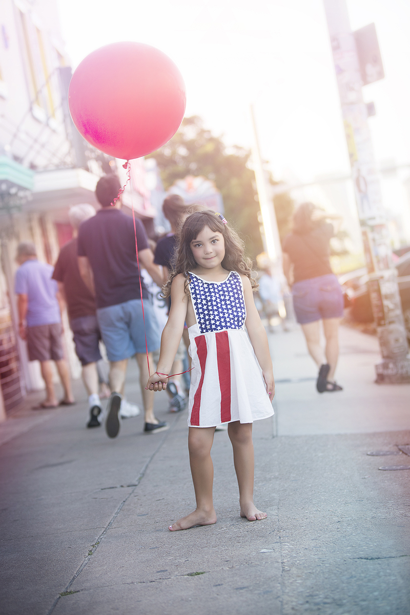 Girl in Patriotic dress holds balloon on city street